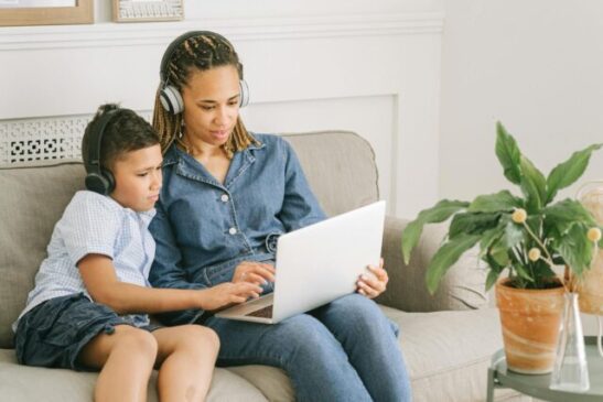 woman in blue and white polka dot button up shirt sitting on gray sofa using macbook